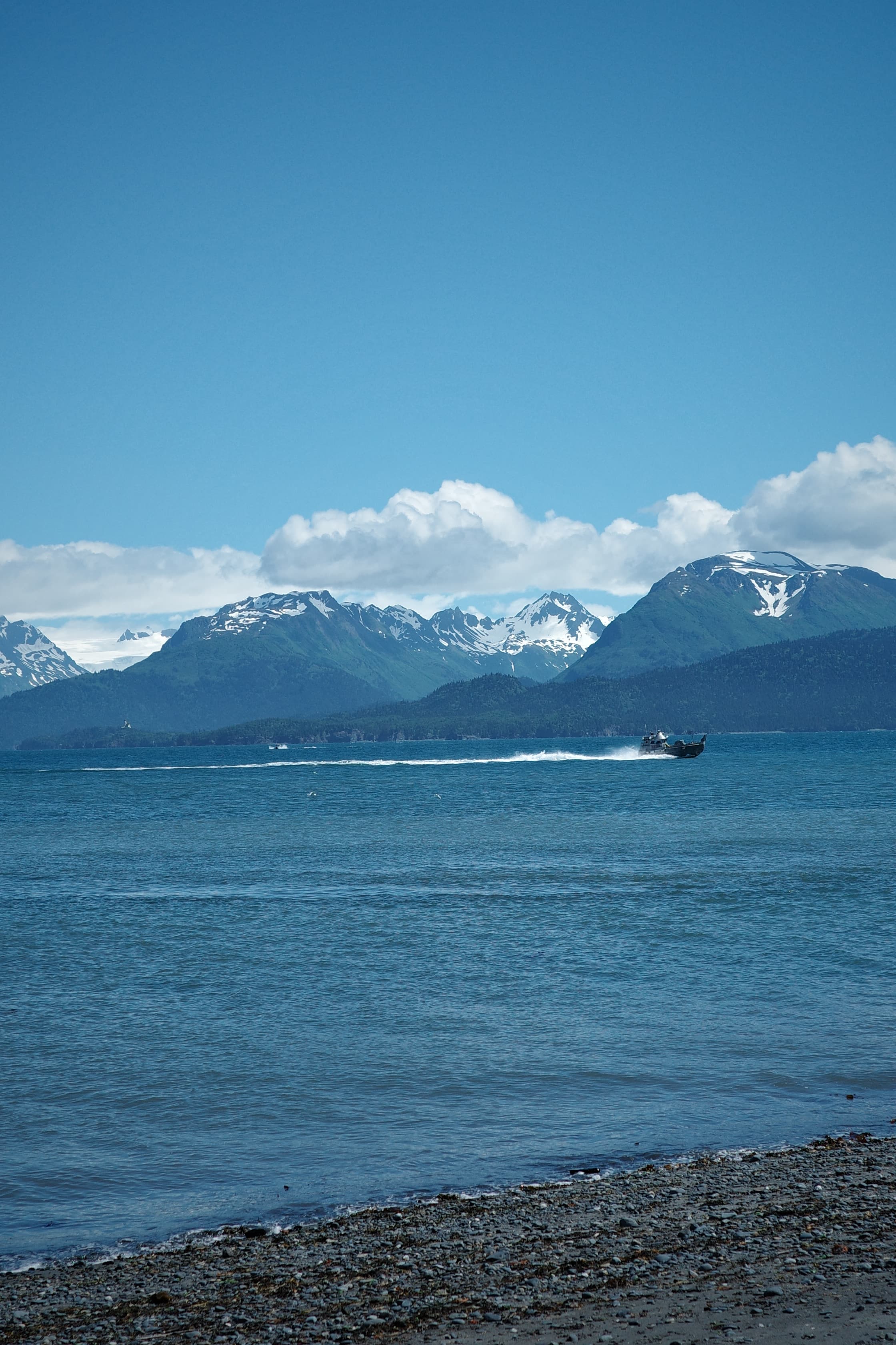 Snowy mountains above a blue bay with a fishing boat and rocky shoreline
